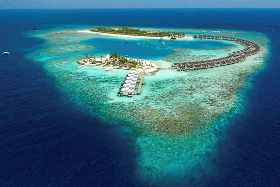 Ilmakuva trooppisesta saaresta, jossa veden yläpuolella olevia bungaloweja ja sininen laguuni, ympäröitynä koralliriutalla. (Tekoälyn luoma teksti)