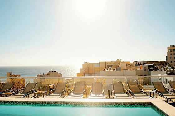 Uima-allas, jossa on aurinkotuoleja, ja taustalla näkyy meri ja rakennuksia. (Tekoälyn luoma teksti)