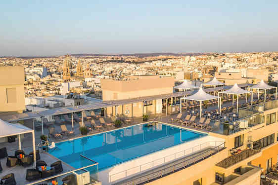 Kuva kattoterassista, jossa on uima-allas, aurinkotuoleja ja taustalla näkyvä kaupunkinäkymä. (Tekoälyn luoma teksti)