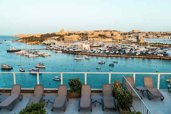 Näkymä satamaan, jossa on veneitä, sekä terassi, jossa on aurinkotuoleja. (Tekoälyn luoma teksti)