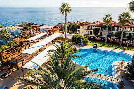 Näkymä hotellialueelle, jossa on uima-allas, palmuja ja meri taustalla. (Tekoälyn luoma teksti)