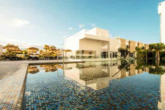 Uima-allasalue, jossa on aurinkovarjoja ja valkoisia rakennuksia. (Tekoälyn luoma teksti)