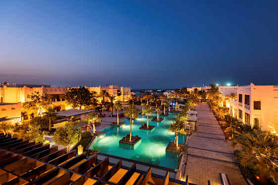 Valaistu lomakohde, jossa on uima-altaita ja palmuja illalla. (Tekoälyn luoma teksti)