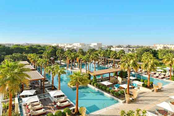 Ylellinen allasalue, jota ympäröi vehreys ja palmut, aurinkotuoleilla ja päivänvarjoilla. (Tekoälyn luoma teksti)