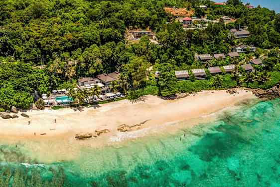 Ranta turkoosilla vedellä, vehreän kasvillisuuden ja rakennusten ympäröimänä. (Tekoälyn luoma teksti)