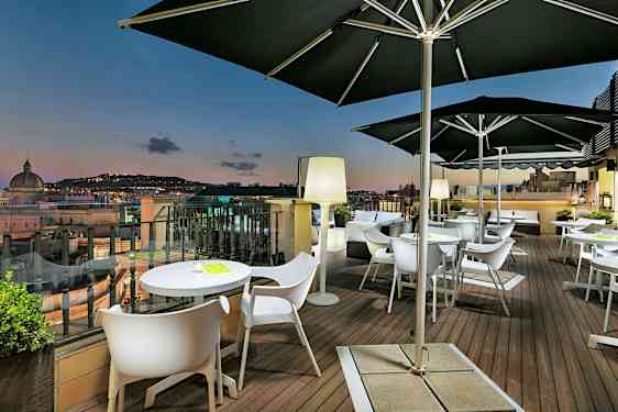 Terassi, jossa on pöytiä ja tuoleja, sekä näköala kaupunkiin hämärän valossa. (Tekoälyn luoma teksti)