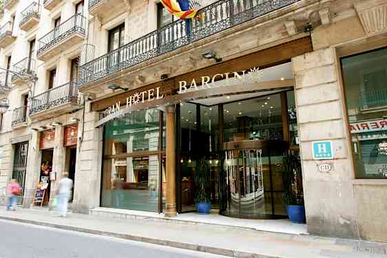 Hotelli, jossa on lasiovi ja koristeellinen kyltti yllä, sijaitsee kadun varrella, jossa on jalkakäytävä. (Tekoälyn luoma teksti)