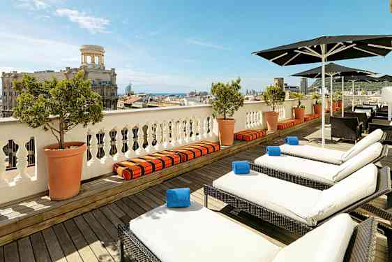 Näköala terassille, jossa aurinkotuoleja ja aurinkovarjoja, taustalla kaupunki ja meri. (Tekoälyn luoma teksti)