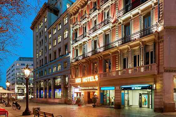 Kaupungin katu hämärässä, jossa valaistuja rakennuksia. Hotellin kyltti loistaa kirkkaasti julkisivussa. (Tekoälyn luoma teksti)