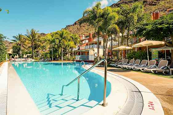 Ulkouima-allas, jonka äärellä aurinkotuoleja hotellin luona, ympäröitynä palmuilla ja vihreillä kasveilla. (Tekoälyn luoma teksti)