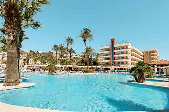 Kuva uima-allasalueesta, jossa on aurinkotuoleja, aurinkovarjoja ja palmuja hotellin edustalla. (Tekoälyn luoma teksti)