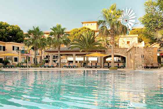 Uima-allas rakennuksen edessä, jossa on palmuja ja pieni tuulimylly näkyvissä. (Tekoälyn luoma teksti)