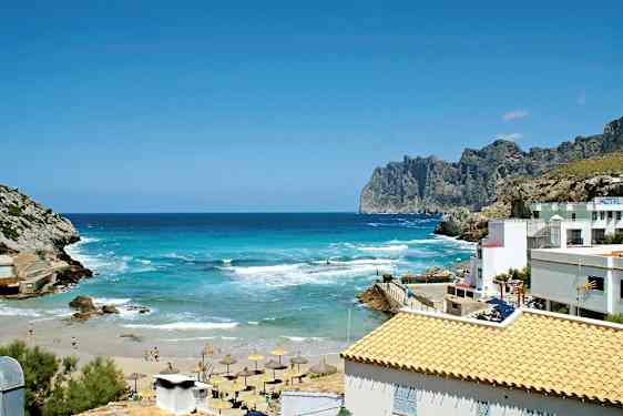 Kaunis rannikko turkoosilla merellä, hiekkaranta ja aurinkovarjoja. Kallioita ja rakennuksia vaaleilla katoilla. (Tekoälyn luoma teksti)