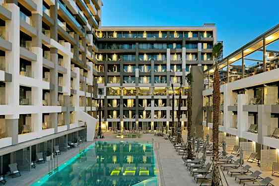 Moderni hotellirakennus, jossa on parvekkeita ja valaistu uima-allas aurinkotuoleineen. (Tekoälyn luoma teksti)