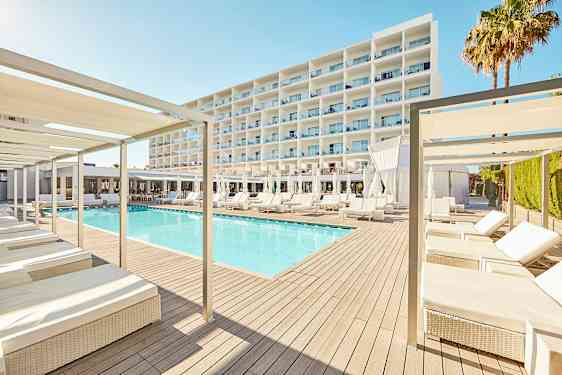 Moderni hotellikohde, jossa on uima-allas aurinkotuolien ja varjojen ympäröimänä, taustalla suuri valkoinen rakennus. (Tekoälyn luoma teksti)