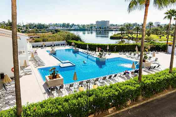 Ulkoallas aurinkotuoleineen ja aurinkovarjoineen, ympärillä vihreitä kasveja ja näkymä järvelle ja avoimeen maisemaan. (Tekoälyn luoma teksti)