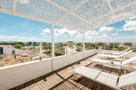 Kattoterassi aurinkotuoleilla ja pöydällä. Terassilla on rei’itetty katos ja lasikaide, josta on näkymä kaupungille ja merelle. (Tekoälyn luoma teksti)