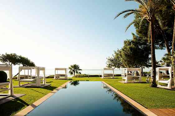 Loputon uima-allas nurmikolla ja valkoisilla aurinkovuoteilla, joista on näkymä merelle. (Tekoälyn luoma teksti)