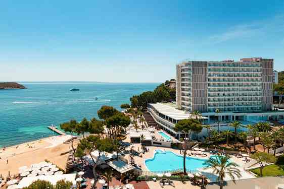 Ilmakuva hotellikompleksista meren rannalla, jossa on uima-altaita, vehreyttä ja ranta. (Tekoälyn luoma teksti)