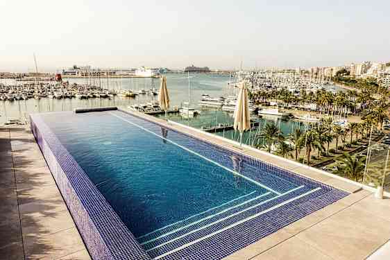 Kuva infinity-altaasta, josta on näkymä venesatamaan, jossa on palmuja ja useampikerroksisia rakennuksia taustalla. (Tekoälyn luoma teksti)