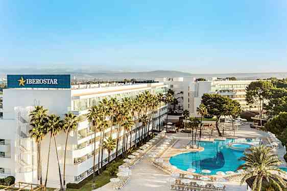 Moderni hotelli palmujen ympäröimänä, jossa on suuri, kirkkaansininen uima-allas. (Tekoälyn luoma teksti)