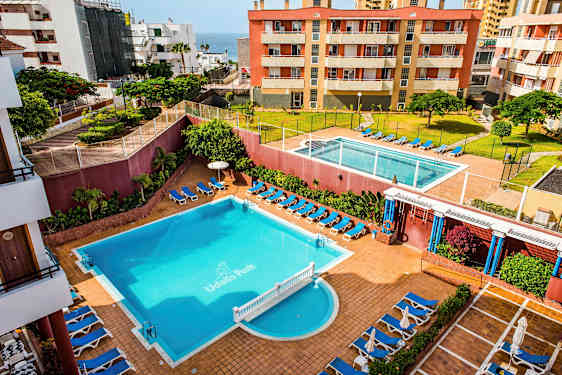 Hotellialue, jossa on kaksi uima-allasta, aurinkotuoleja ja ympäröiviä rakennuksia. (Tekoälyn luoma teksti)