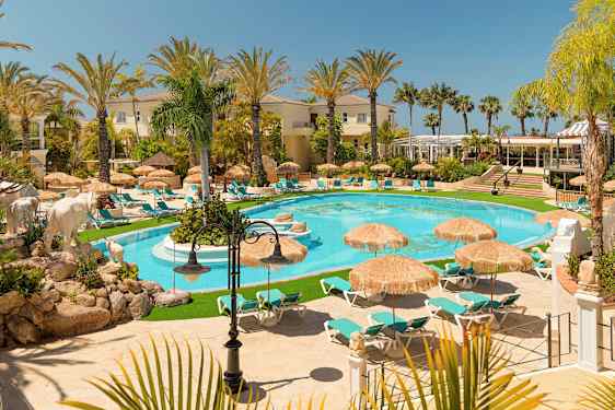 Kuva ylellisestä lomakohteesta, jossa on uima-allas aurinkotuolien ja aurinkovarjojen ympäröimänä, palmuja ja rakennuksia ympärillä. (Tekoälyn luoma teksti)