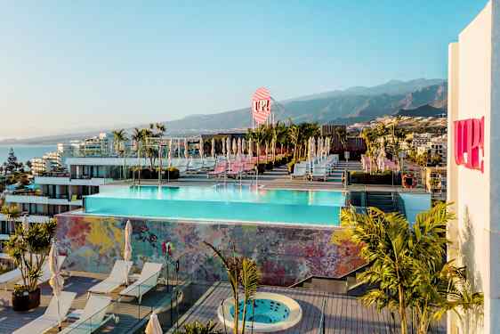 Suuri kattoterassi, jossa on uima-allas, aurinkotuoleja ja kasveja. Taustalla vuoria ja rakennuksia. (Tekoälyn luoma teksti)