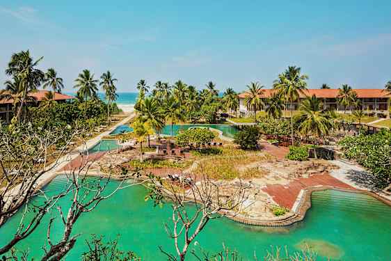 Hotellikompleksi uima-altaineen, palmuineen ja hiekkarantoineen taustalla. (Tekoälyn luoma teksti)