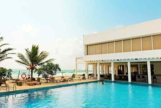 Ulkouima-allas, jonka vierellä on aurinkotuoleja ja palmuja modernin hotellin vieressä meren äärellä. (Tekoälyn luoma teksti)