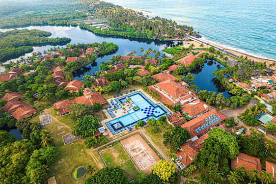 Ilmakuva lomakohteesta, jossa on terrakotanväriset katot, suuri uima-allas ja ympäröivä vehreys. (Tekoälyn luoma teksti)