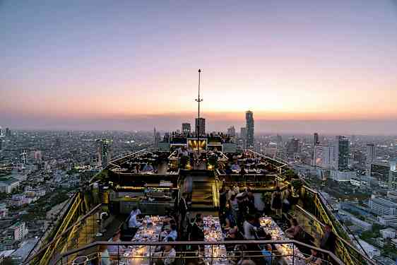 Kattoterassi auringonlaskun aikaan ravintola-asiakkaiden ja kaupungin maisemien kanssa. (Tekoälyn luoma teksti)