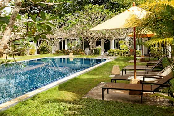 Uima-allas viheralueineen ja aurinkotuoleineen, taustalla rivi valkoisia rakennuksia. (Tekoälyn luoma teksti)