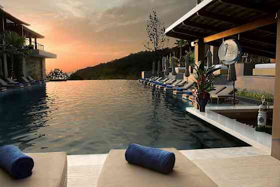 Infinity-allas, jossa on aurinkotuoleja ja pyyhkeitä lomakohteessa auringonlaskun aikaan. (Tekoälyn luoma teksti)