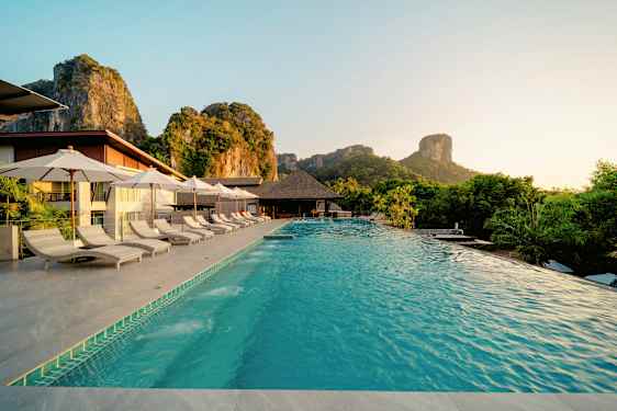 Uima-allas, jossa on aurinkotuoleja ja varjoja, sijaitsee lomakohteessa luonnonkauniilla alueella vuorien ympäröimänä. (Tekoälyn luoma teksti)