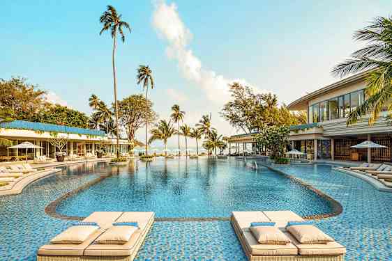 Suuri ulkouima-allas, jota ympäröivät aurinkotuolit, palmut ja rakennukset, näkymä merelle. (Tekoälyn luoma teksti)