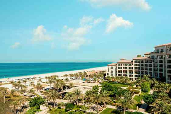 Näköala lomakohteeseen meren rannalla, etualalla rakennus ja vihreää sekä palmuja. (Tekoälyn luoma teksti)