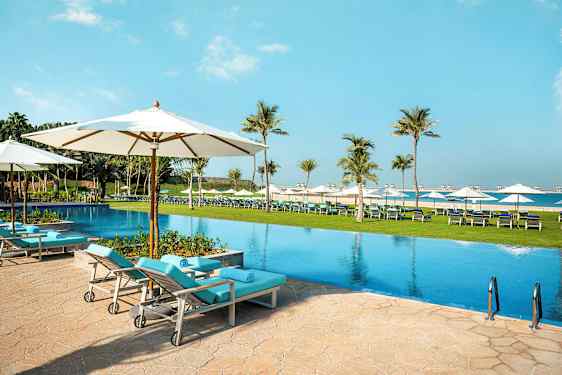 Uima-allas aurinkotuoleineen ja varjoineen ulkoilmassa, ympäröitynä palmuilla ja nurmialueella. (Tekoälyn luoma teksti)