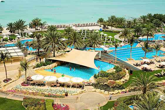 Lomakohde, jossa allasalue lähellä rantaa, ympäröitynä palmuilla ja aurinkotuoleilla. (Tekoälyn luoma teksti)