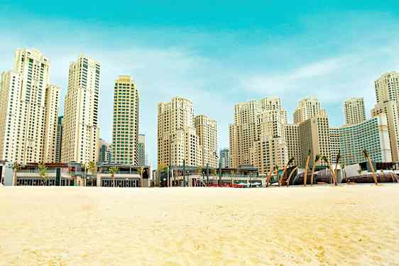 Ranta, jonka edustalla on hiekkaa ja taustalla korkea, moderni rakennus. (Tekoälyn luoma teksti)