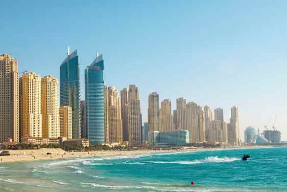 Kuva korkeista rakennuksista rannalla ja kirkkaan sinisestä vedestä, lähellä rantaa on henkilö vesiskootterilla. (Tekoälyn luoma teksti)