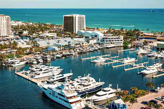 Venesatama ylellisine jahteineen ja veneineen kaupunkirakennusten ja viheralueiden vieressä, taustallaan meri. (Tekoälyn luoma teksti)