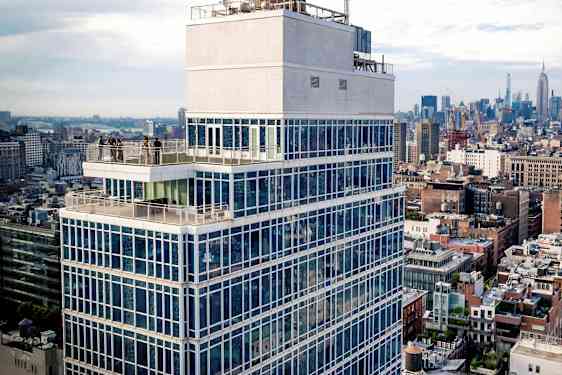 Korkea rakennus lasijulkisivulla ja terassilla, kaupunkimaiseman ympäröimänä. (Tekoälyn luoma teksti)