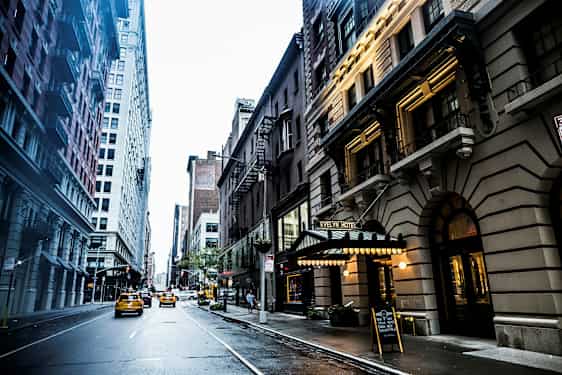 Kaupunkikatu, jonka molemmin puolin on korkeita rakennuksia, ja tiellä liikkuu takseja. Evelyn-hotellin kyltti näkyy oikealla. (Tekoälyn luoma teksti)