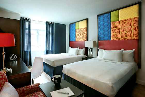 Hotellihuone, jossa on kaksi sänkyä, modernit huonekalut ja koristeellisia yksityiskohtia. (Tekoälyn luoma teksti)