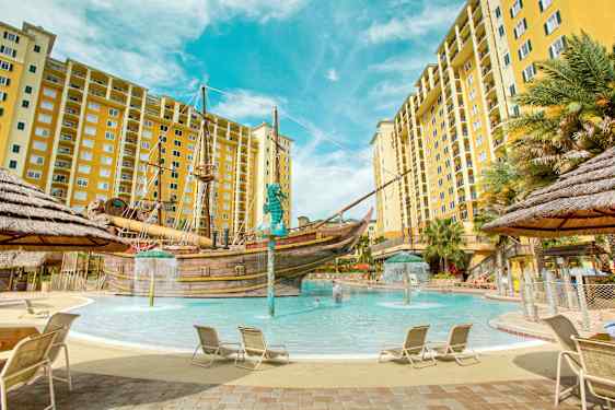 Uima-allas, jota ympäröivät aurinkotuolit ja keltaiset kerrostalot, keskellä merirosvolaiva. (Tekoälyn luoma teksti)