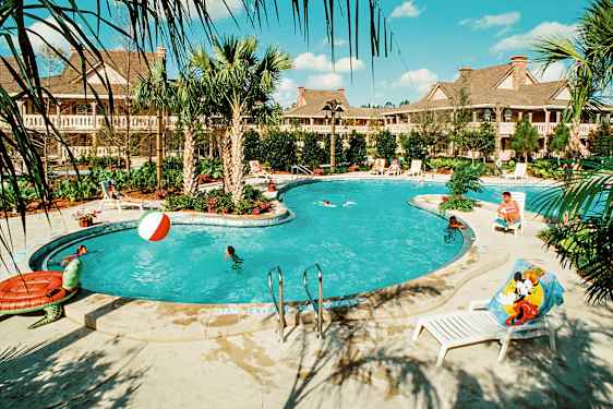 Ulkouima-allas, jonka ympärillä on palmuja ja aurinkotuoleja, joissa ihmiset uivat ja leikkivät vedessä. Taustalla näkyy rakennuksia. (Tekoälyn luoma teksti)