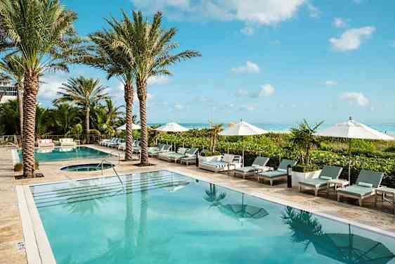 Kuva hotellin uima-allasalueesta, jossa on palmuja, aurinkotuoleja ja varjoja. Taustalla näkyy meri. (Tekoälyn luoma teksti)