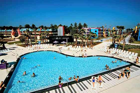 Uima-allas, jota ympäröivät aurinkotuolit lomakohteessa. Taustalla rakennuksia ja koristuksia. (Tekoälyn luoma teksti)