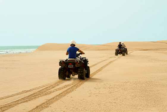 Kaksi henkilöä ajaa mönkijöillä hiekkarannalla, meri taustalla. (Tekoälyn luoma teksti)